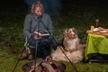 Australian Shepherd dog is lying by the campfire, the kettle with food is cooking and steaming, The woman is reading a book, Royalty Free Stock Photo