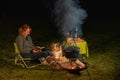 Australian Shepherd dog is lying by the campfire, the kettle with food is cooking and steaming, The woman is reading a Royalty Free Stock Photo