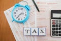 Australian tax forms with calculator, pen and blue alarm clock on the table. View from above. Tax concept. The word tax on cubes