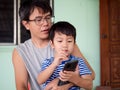 Authentic asian child boy and father watching to mobile phone together. Royalty Free Stock Photo