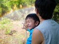 Authentic asian child boy smiling with happy face while making beautiful rainbow with father by water, sunlight