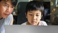 Authentic asian child boy using laptop with father with serious face.