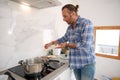 Handsome young man putting chopped garlic from cutting board into a saucepan with boiling tomato sauce, cooking at home Royalty Free Stock Photo