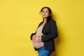 Gorgeous pregnant woman expecting baby, forming a heart shape with her fingers on her belly, isolated yellow background