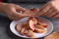 Authentic female hands holding a piece of a fresh cutting ripe peach on white plate