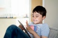 Authentic Kid sitting on sofa watching cartoons or playing games on tablet,Child boy using digital pad learning lesson on internet Royalty Free Stock Photo