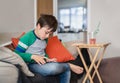 Authentic Kid sitting on sofa watching cartoons or playing games on tablet,Child boy using digital pad learning lesson on internet Royalty Free Stock Photo