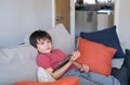 Authentic Kid sitting on sofa watching cartoons or playing games on tablet,Child boy using digital pad learning lesson on internet Royalty Free Stock Photo