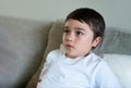 Authentic Kid sitting on sofa watching TV, Emotional portrait Young boy siting on sofa looking out with thinking face or nervous, Royalty Free Stock Photo