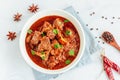 Lamb Curry / Lamb Vindaloo in a Bowl on White Background with Scattered Raw Spices