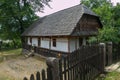 Authentic old Ukrainian hut with a tall wooden fence against the backdrop of a green garden with trees Royalty Free Stock Photo