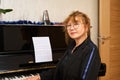 Authentic portrait of Asian mature woman piano teacher in casual clothes and eyeglasses, confidently looking at camera