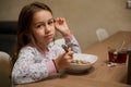 Authentic portrait of a beautiful Caucasian little child girl enjoys eating cereal for morning breakfast with appetite. Royalty Free Stock Photo