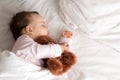 Authentic portrait cute caucasian little infant chubby baby girl or boy in pink sleep with teddy bear on white bed Royalty Free Stock Photo