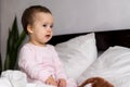 Authentic portrait cute caucasian little infant chubby baby girl or boy in pink sleepy upon waking looking at camera in