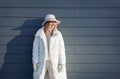 Authentic portrait of laughing blonde Woman on gray background with shadow from the sun, in winter warm white clothes looking away