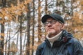 An authentic portrait of serious, unshaven middle-aged man in glasses and cap against the background of an autumn forest Royalty Free Stock Photo