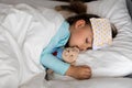 Authentic portrait sick cute caucasian little preschool baby girl in blue sleep with compress on forehead on white bed