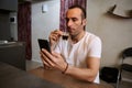 Authentic portrait of young Caucasian handsome man drinks coffee and reads news, sitting at table in the home interior Royalty Free Stock Photo