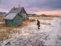 Authentic Russian northern village, old dilapidated wooden houses, harsh Arctic nature. A man with a bucket of water goes to his