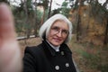 Authentic selfie portrait of attractive elderly 60 year old woman with gray hair and eyeglasses in nature forest or park