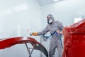 Car painter in protective clothes and mask painting automobile bumper with metallic paint and varnish in chamber Royalty Free Stock Photo