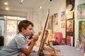 Authentic talented inspired teenager boy learning art and painting on canvas in the exhibition hall of art gallery Royalty Free Stock Photo