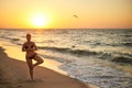 Authentic woman in swimsuit doing yoga vrikshasana on the beach in the morning. Real unretouched shape girl silhouette