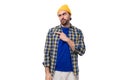 authentic young european brunette man with brutal beard and mustache dressed in yellow hat and blue shirt thinking