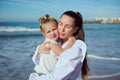 Authentic young happy affectionate mother gently hugs her adorable little child daughter, walking together on the beach Royalty Free Stock Photo