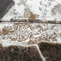 An aerial view on an East European field with partially melted snow, trenches and woods