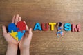 Autistic boy hands holding heart shapeed puzzle with word autism and awarennes ribbon on wooden background. Autism Royalty Free Stock Photo