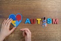 Autistic boy hands holding heart shapeed puzzle with word autism and awarennes ribbon on wooden background. Autism Royalty Free Stock Photo