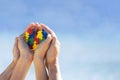 Autistic kid hands with multicolored puzzle heart supported by mother hands over blue sky background. World autism Royalty Free Stock Photo