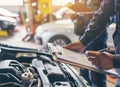 Auto check, car service shop concept. Automobile repairman writing job checklist on clipboard, mechanic checking engine Royalty Free Stock Photo