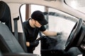 Auto cleaning service and detailing concept. Handsome Caucasian man in black uniform cleaning interior of the car with Royalty Free Stock Photo