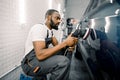 Auto detailing service, polishing of the car. Side view of young African American man worker n t-shirt and overalls Royalty Free Stock Photo