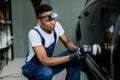 Auto detailing service, polishing of the car. Side view of young African American man worker in t-shirt and overalls Royalty Free Stock Photo
