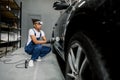 Auto detailing service, polishing of the car. Side view of young African American man worker in unifrom, t-shirt and Royalty Free Stock Photo