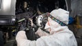 An auto mechanic applies anti-corrosion mastic to the underbody of a car.