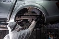 An auto mechanic applies anti-corrosion mastic to the underbody of a car.