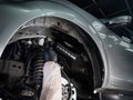 An auto mechanic applies anti-corrosion mastic to the underbody of a car.