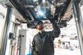 Auto mechanic with LED work light inspecting car chassis standing under it Royalty Free Stock Photo