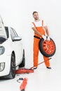 auto mechanic in orange uniform carrying car tire