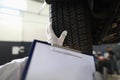 Auto mechanic technician holds blank clipboard sheet in hand with copy space text and car tires Royalty Free Stock Photo