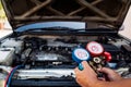 Auto mechanic using measuring equipment for filling car air conditioners checking.