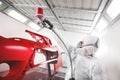 Auto mechanic worker painting car element with spray gun in a paint chamber during repair work. Royalty Free Stock Photo