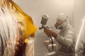 Auto mechanic worker spraying car body to orange gold color using spray gun in a paint chamber during repair work. Royalty Free Stock Photo