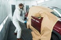 Auto painter in a protective suit and mask sprays a degreaser or other cleaner on a car door using a spray gun. Royalty Free Stock Photo