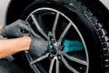 Auto wash service. Cropped close up image of male hands in black protective gloves, cleaning alloy wheels rims of luxury Royalty Free Stock Photo